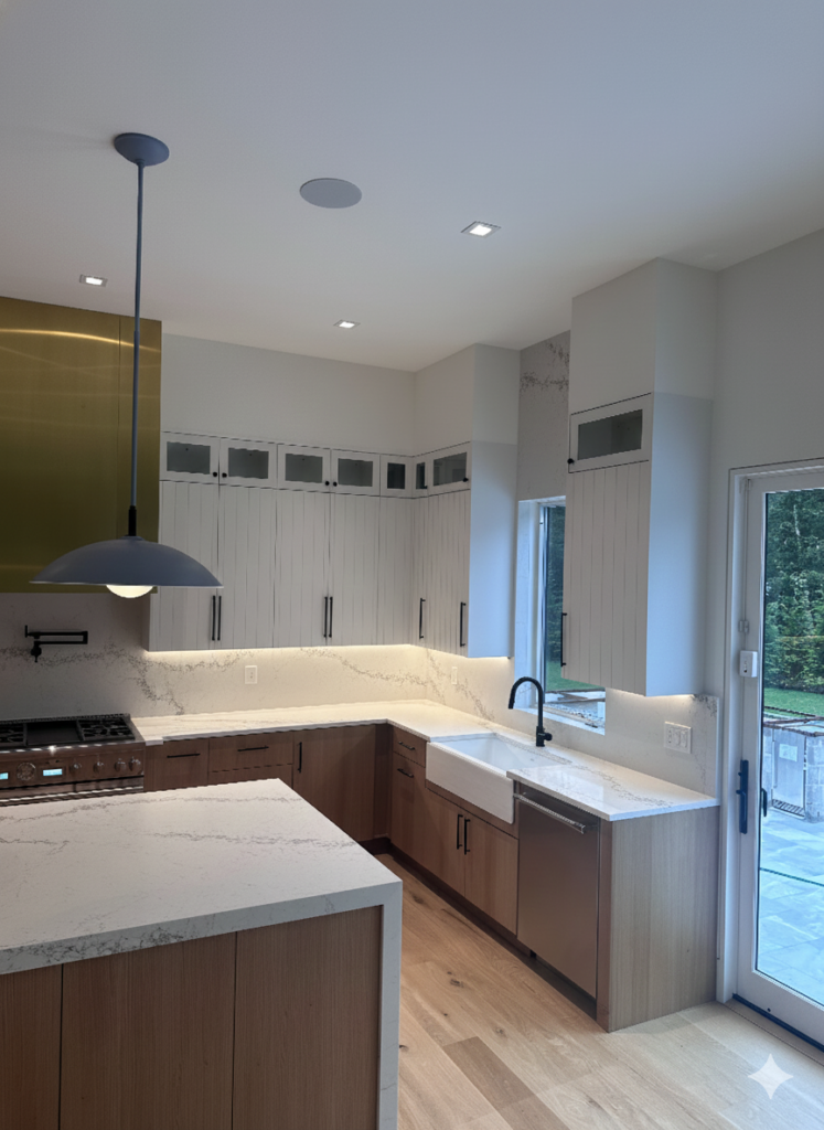 Luxury modern kitchen featuring light wood lower cabinets, white vertical slat upper cabinets, quartz countertops, a farmhouse sink, and a striking brass range hood accent.